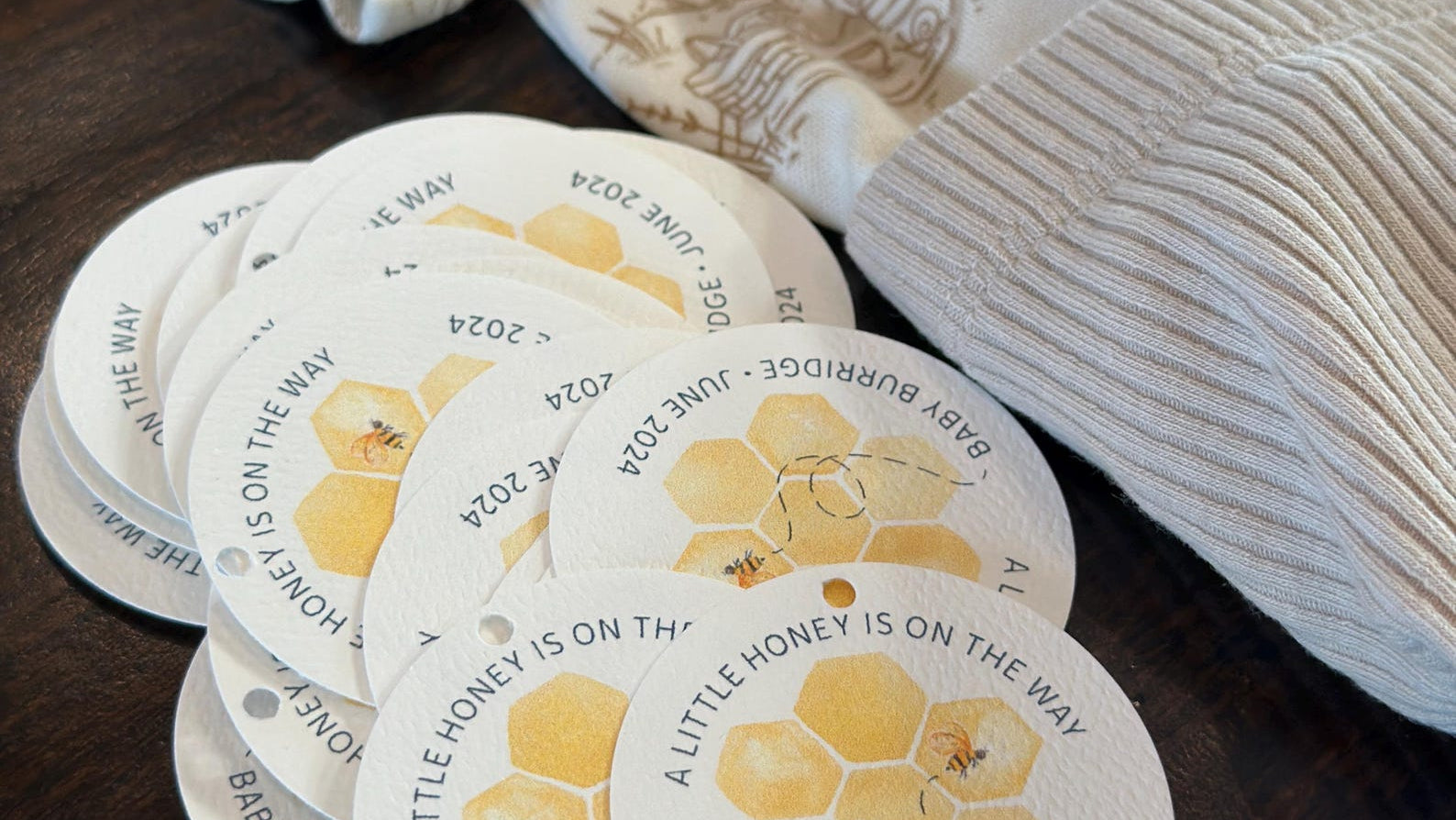 Round baby shower favor labels with honey design on a wooden surface.